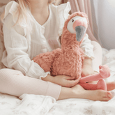 Girl sitting cross legged on a bed with the weighted flamingo propped upright against her