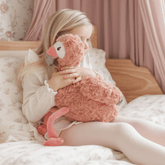 Girl sitting on a bed hugging the weighted flamingo against her chest