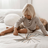 Child sitting on a bed reaching for a pile of scattered pick up sticks