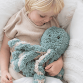 Child resting back against pillows with the teal weighted octopus held on their chest