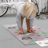 Child bending forward to touch their toes on the grey Nature mat, with a yoga card beside them