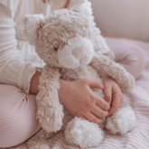 Child sitting on a bed with the cream weighted cat propped beside them
