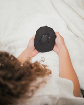 A child lying in bed, holding a black Zenimal+ above them in both hands.