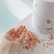 Pink bath salt crystals scattered on a counter beside the Magnesium Calming Soak tub, with a child's hand