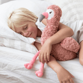 Child lying in bed with their head on a pillow, one arm wrapped around the weighted flamingo