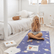 Child sitting cross legged on a space print mat with palms together, yoga cards laid out nearby