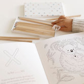 Child's hand lifting colored pencils from the box beside an open coloring page of a koala