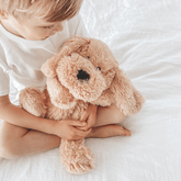Child sitting on a white bed with the weighted puppy held in their lap
