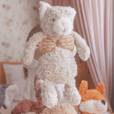 Child holding the weighted cat up by its front paws, with other weighted plush animals on the bed behind