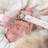 Hands holding a pink flamingo plush and a box of bath fizzies on a muslin blanket.