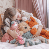 Girl asleep on a bed surrounded by weighted plush animals including the cat, flamingo, octopus and fox
