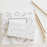 The spotted pencil box resting on an open coloring page, with three pencils alongside
