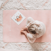 Child sitting cross legged on the pink Rose mat, seen from above, with a yoga card beside them