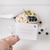 Hand tucking a Love Note reading I love you and I am so proud of you beside a packed lunch box