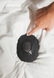 A hand pressing a button on a black Zenimal+ resting on white bedding.