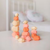 Three towers of coral and cream Patience Pebbles stacked on a table beside a crib