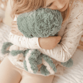Child hugging the teal weighted octopus close, seen from the side