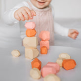 Toddler balancing a coral stacking pebble on top of a tower, with more pebbles scattered on the table