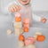 Toddler balancing a coral stacking pebble on top of a tower, with more pebbles scattered on the table
