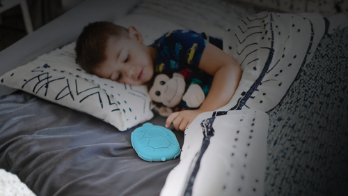 Child sleeping on a bed with a teddy bear and teal Zenimal Kids meditation device
