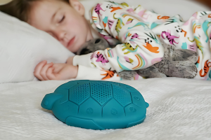 Child sleeping with a teal turtle-shaped Zenimal device for calm and sleep pillow on a bed