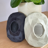 Two Zenimal+ devices, one dark blue and one cream, on a wooden table beside a potted plant.