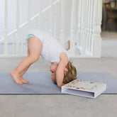 Child in downward dog on the blue grey mat beside an open box of yoga cards