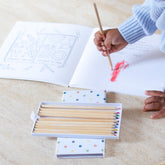 Child coloring in the book with a red pencil, the open pencil box beside them