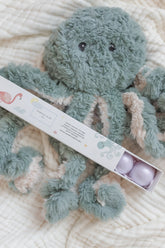 Teal octopus plush on a cream waffle blanket beside an open box of three bath fizzies.