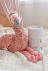 Pink flamingo plush resting on a bed beside a tube of magnesium calming soak.