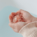 A child's cupped hands holding pink bath salt crystals above a tub of blue water.