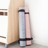Two rolled yoga mats, grey and pink, stored upright beside a wooden cabinet