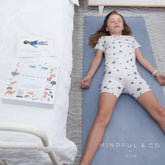 Child lying flat on their back in resting pose on the blue grey mat, with the yoga card box nearby