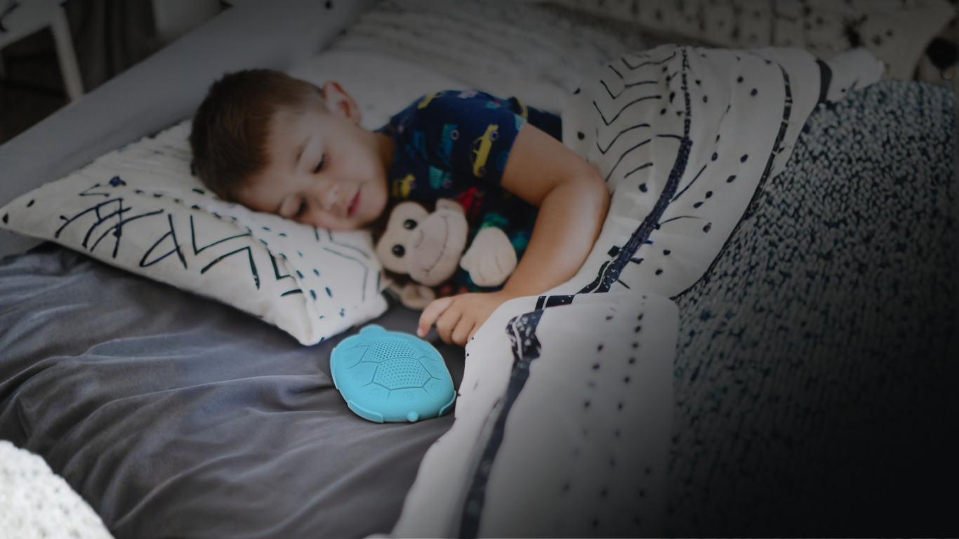 Child sleeping on a bed with a monkey stuffed animal and teal Zenimal kids meditation device, surrounded by pillows and blankets