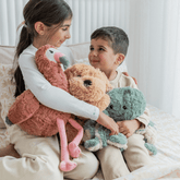Two children sitting on a bed hugging the flamingo, puppy and octopus plush toys.