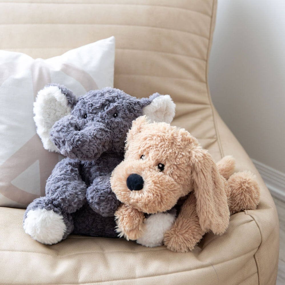 The weighted elephant and the weighted puppy sitting together on a cream armchair
