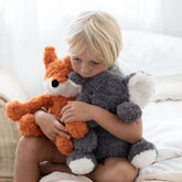 Boy sitting on a bed holding the weighted elephant and an orange weighted fox