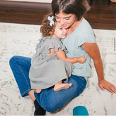Girl holding a sister on a floor with a zenimal on the floor