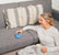 Woman sitting on the floor by a gray sofa, smiling and resting her hand on a blue Zenimal on the cushion while holding a mug