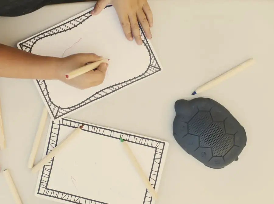 A child draws with colored pencils at a white table, a Zenimal beside the paper
