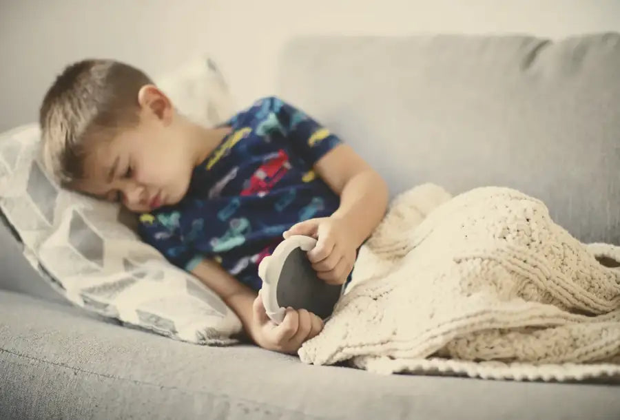 A boy curled up on the sofa under a knit blanket, eyes closed, holding his Zenimal