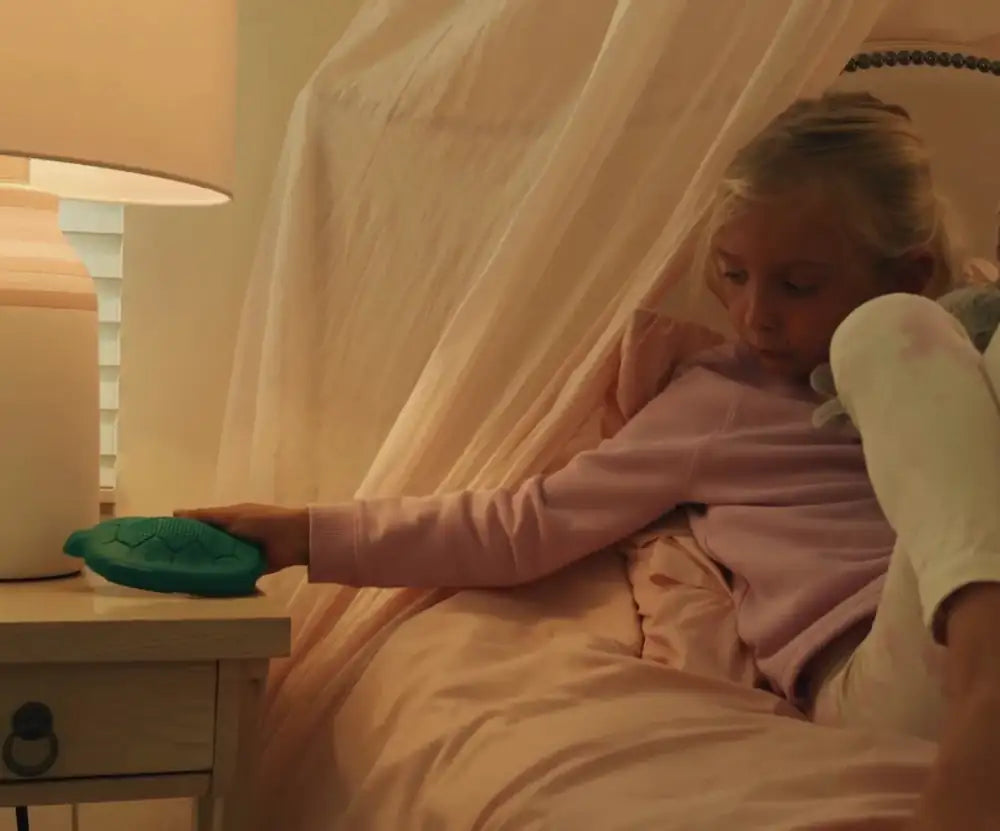 At bedtime, a girl in pink pajamas reaches from her canopy bed to set her Zenimal on the nightstand beside the lamp